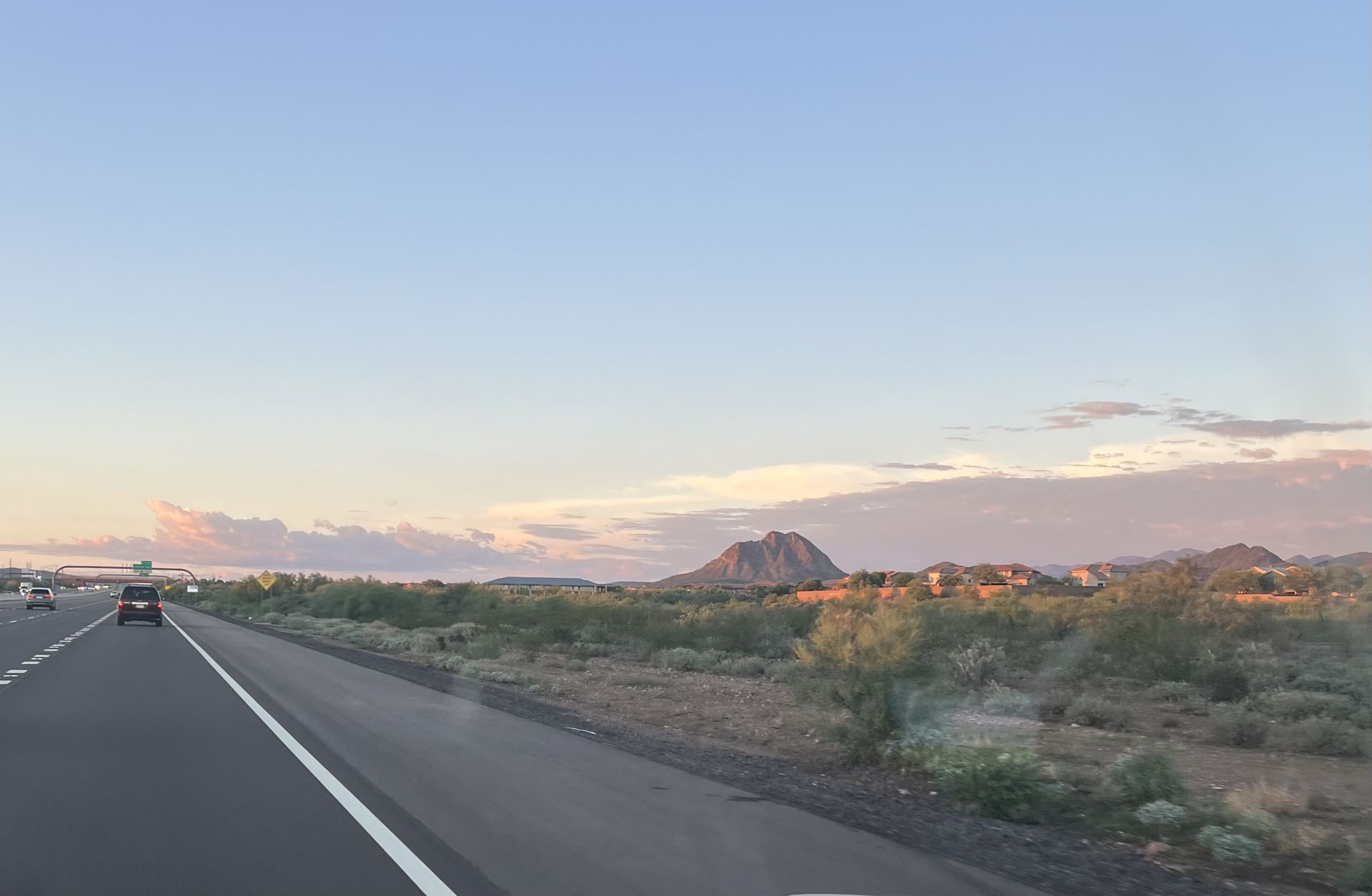 I-17 heading north at sunset, with desert brush, a peak and the rooftops of Anthem homes to the right of the freeway