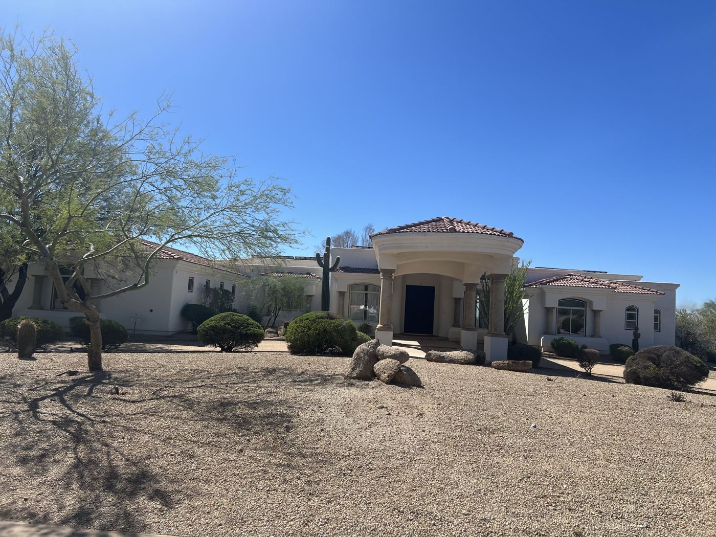 A white single-story desert home with a tile roof and gravel front yard